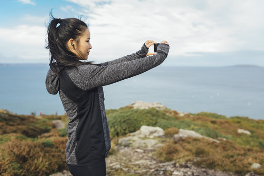 Ireland, Howth, female athlete taking cell phone picture at cliff coast
