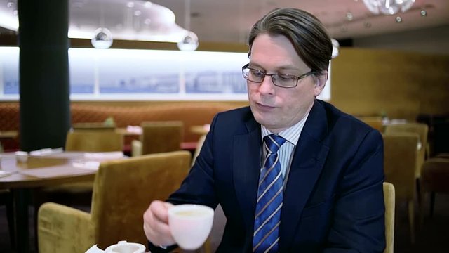 А businessman drinking a coffee in a hotel cafe before a business meeting. Slow motion.