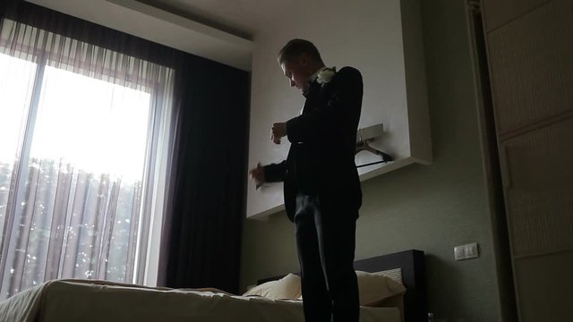 Young man  puts on his jacket in light room. Stylish man in a fashion suit costume preparing to go out at a reception or wedding.