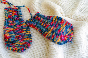 Two multicolored knitted mittens on white scarf