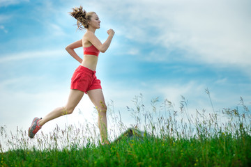 Young lady running. Woman runner running through the summer park rural road. Workout in a park. Beautiful fit girl. Fitness model caucasian ethnicity outdoors. Weight loss exercise. Jogging.