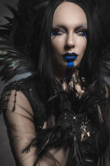 Young woman in black fantasy costume with feathers on dark background