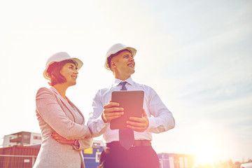 happy builders in hardhats with tablet pc outdoors