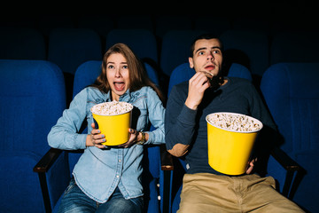 Cinema day,  young couple with popcorn looking horror movie in cinema at their date.