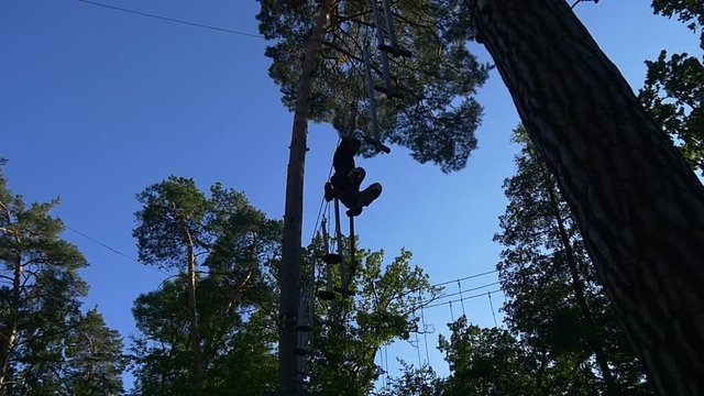 Tourist Silhouette in Adventure Rope Park Young Man Has Fun on Rope Road in Summer Sunny Day Occupied by Sport Firest Blue Sky Tourism in Ukraine