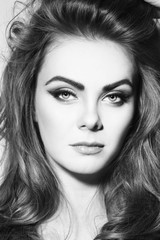 Fototapeta premium Black and white portrait of young beautiful girl with stylish winged eye make-up and long curly hair