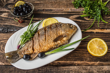 Grilled fish on brown plate with herbs and lemon  old wooden background, top view. Mediterranean luxurious seafood concept.