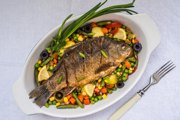 Grilled fish on brown plate with herbs and lemon  white background, top view. Mediterranean luxurious seafood concept.