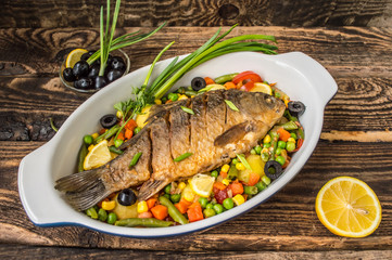 Grilled fish on brown plate with herbs and lemon  old wooden background, top view. Mediterranean luxurious seafood concept.