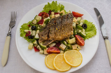 Fried fish fillet on a bed of Caesar salad. Wooden background. Top view.