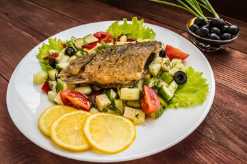 Fried fish fillet on a bed of Caesar salad. Wooden background. Top view.