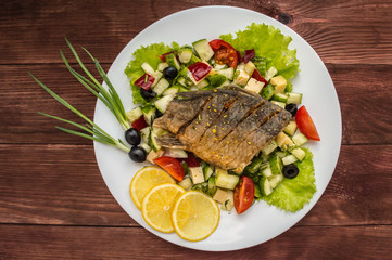 Fried fish fillet on a bed of Caesar salad. Wooden background. Top view.