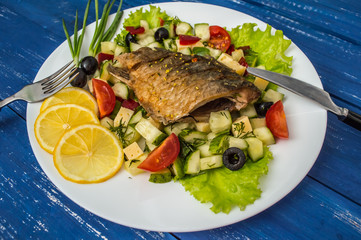Fried fish fillet on a bed of Caesar salad. Wooden background. Top view.