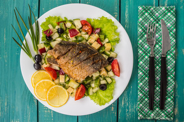 Fried fish fillet on a bed of Caesar salad. Wooden background. Top view.