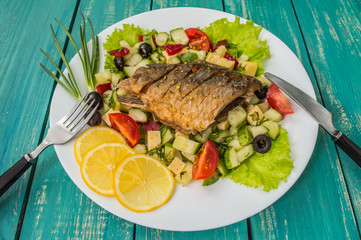 Fried fish fillet on a bed of Caesar salad. Wooden background. Top view.