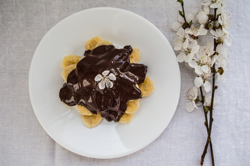 Bananas covered with chocolate on a white plate. Top view