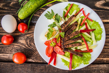 Salad of roasted meat, lettuce, boiled eggs, paprika, tomato and cucumber on a wooden table. Top view