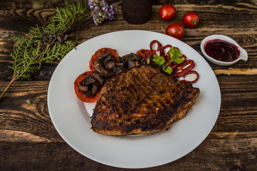 Grilled steak with mushrooms, tomatoes and peppers on a white plate. Wooden background