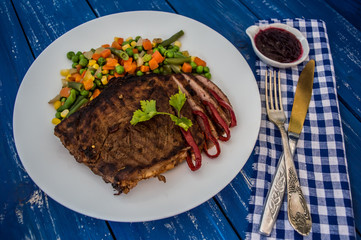 Grilled steak with steamed vegetables on a white plate. blue table. Top view