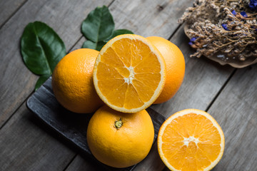 Macro view of vibrant, yellow lemon slice and two whole lemons on dark brown, rustic, wooden table