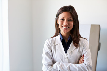 Portrait Of Female Doctor Wearing White Coat In Exam Room - obrazy, fototapety, plakaty