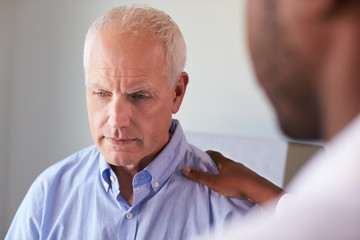 Doctor Talking To Unhappy Male Patient In Exam Room