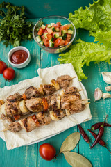 Pork cooked with vegetables on skewers  a turquoise table. Wooden background