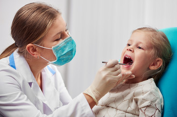Woman dentist in mask doing teeth checkup of little girl in dental room. Health care and medicine...