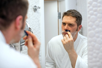 Handsome man shaving in bathroom.