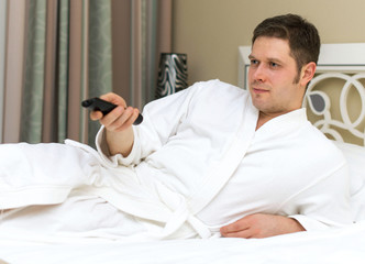 Man in bathrobe watching TV in hotel room.