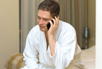 Man in bathrobe with mobile phone in hotel room.