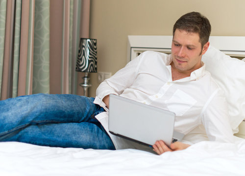Handsome man using laptop in hotel room.