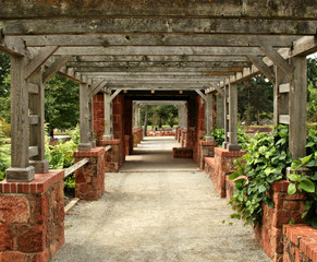 Weathered wood and brick rock arbor creates a tunnel in  a green garden
