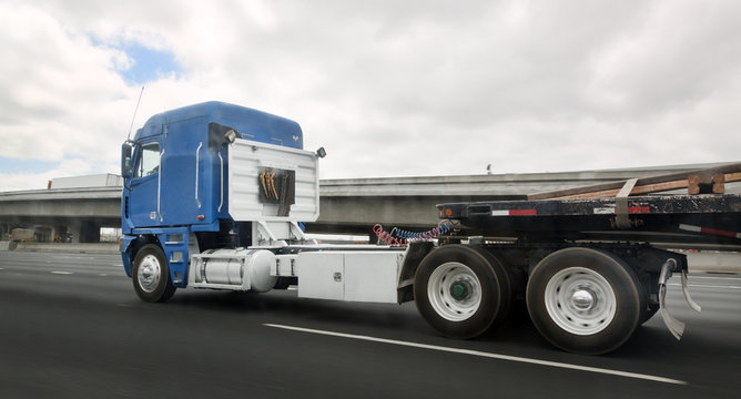 Side view of blue cab flatbed semi on highway under cloudy sky. Horizontal.