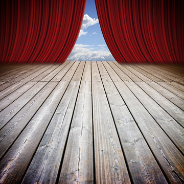 Open theater red curtains and wooden floor against a cloudy sky