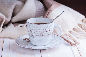 Fototapeta na wymiar vintage mug with hot coffee and spices decorated with a blanket in cage on a white wooden surface