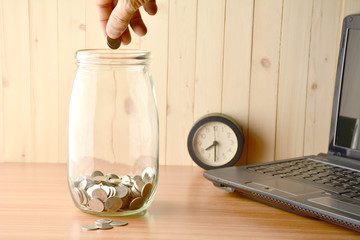 Person drop coins into the bottle, alarm clock and laptop on the table.