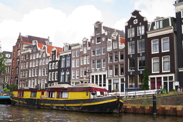 Naklejka premium Yellow houseboat and traditionsl houses - Amsterdam - Netherlands