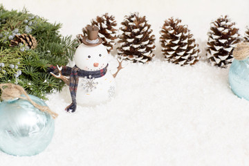 Christmas tree branches and snowman are in the snow. Christmas light background has cones.