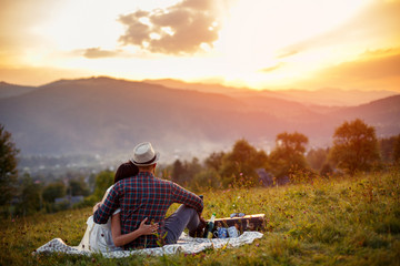 Naklejka na ściany i meble happy loving couple sitting on plaid in field. background mountains.