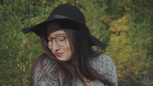 Portrait of young pretty smiling woman in black hat and glasses on the autumn street