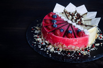 Delicious raspberry cake with fresh raspberries, blueberry, almond slices, rose pepper and chocolate cheesecake on black background.