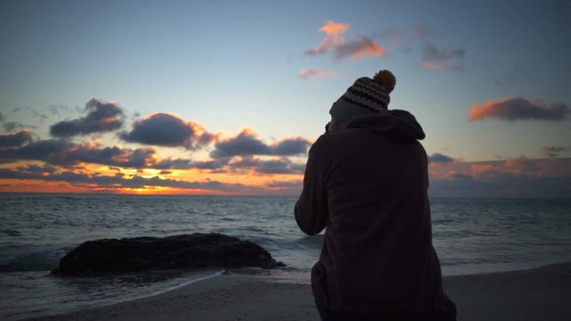 Young handsome man taking a photo of a beautiful sunset on the beach slow motion
