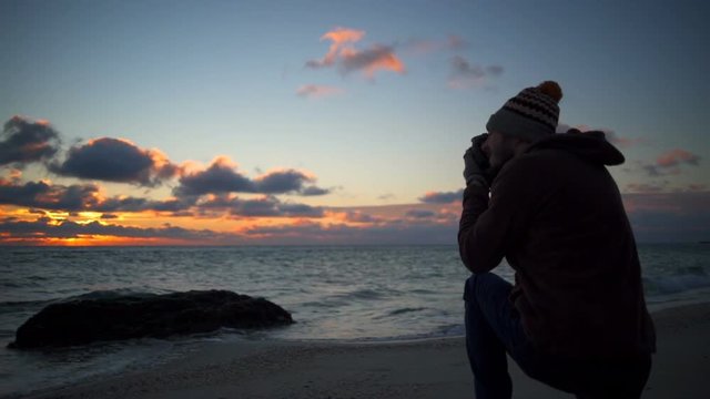 Young handsome man taking a photo of a beautiful sunset on the beach slow motion