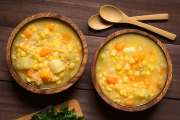 Vegetarian and vegan yellow split pea soup or stew with potato, carrot and celery in wooden bowls,...