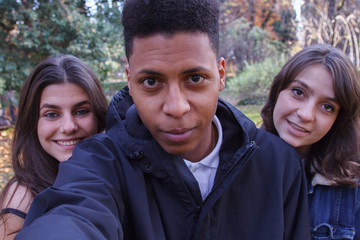 Young people of different races taking a selfie with the smartphone in the park. They are friends and enjoy a nice day outdoors. 