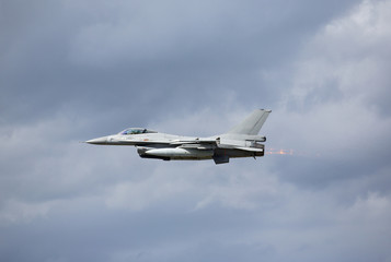 Military jet fighter flying low on a cloudy day. Image taken near an airport.