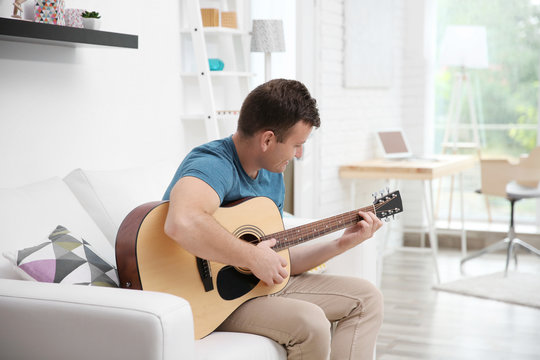 Young man playing the guitar on the sofa in light room