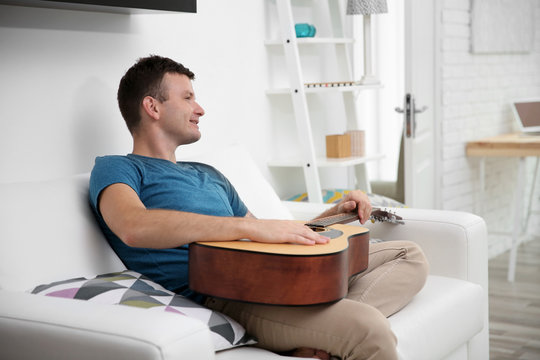 Young man playing the guitar on the sofa in light room