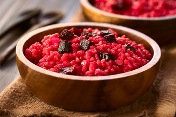 Rote Beete Risotto mit pürierter rote Beete, garniert mit gebackener Beete, serviert in Holzschüssel, fotografiert mit natürlichem Licht (Selektiver Fokus, Fokus in die Mitte des Risottos)
